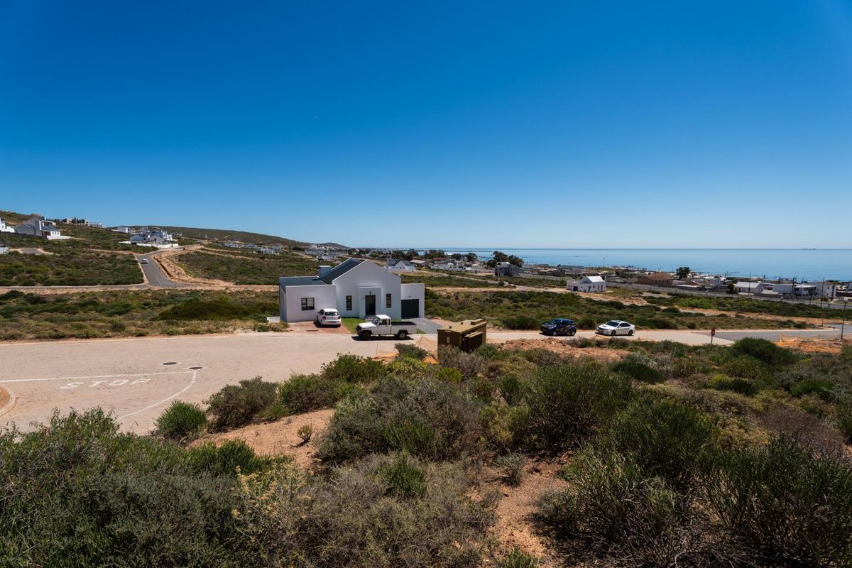 An elevated aerial view of a residential coastal area featuring natural vegetation, paved roads, and distant ocean views.