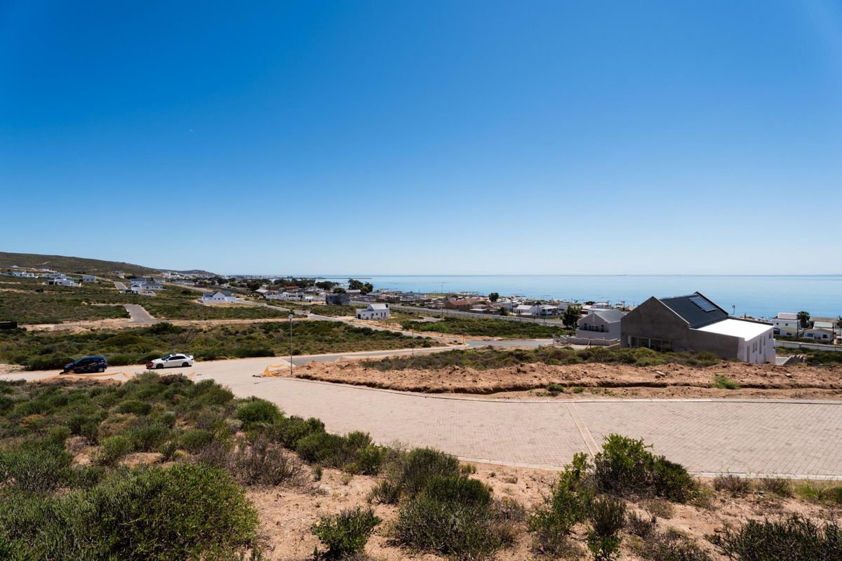An elevated view overlooking the coastal residential area, showcasing the surrounding landscape, paved access roads, and proximity to the ocean.