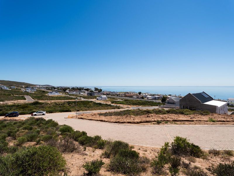 An elevated view overlooking the coastal residential area, showcasing the surrounding landscape, paved access roads, and proximity to the ocean.
