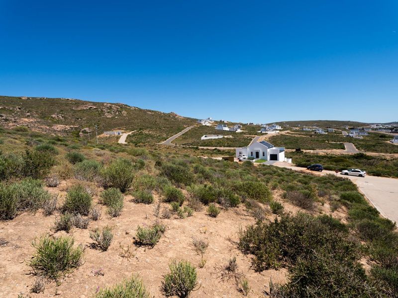 An elevated aerial view of a vacant residential plot featuring natural coastal vegetation and access to a paved road in a quiet neighborhood.