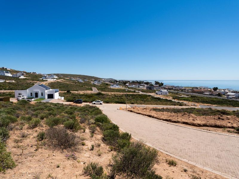 An elevated aerial view of a vacant residential plot featuring paved road access and scenic coastal views in a developing neighbourhood.