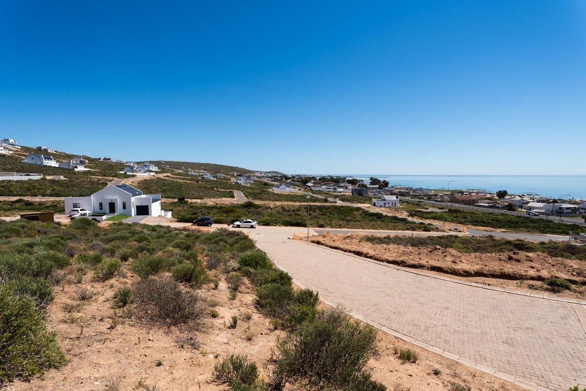 An elevated aerial view of a vacant residential plot featuring paved road access and scenic coastal views in a developing neighbourhood.