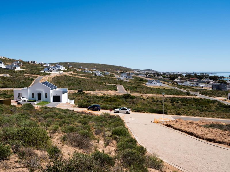 An elevated aerial view of a residential estate featuring paved roads and surrounding coastal landscape with nearby housing developments.