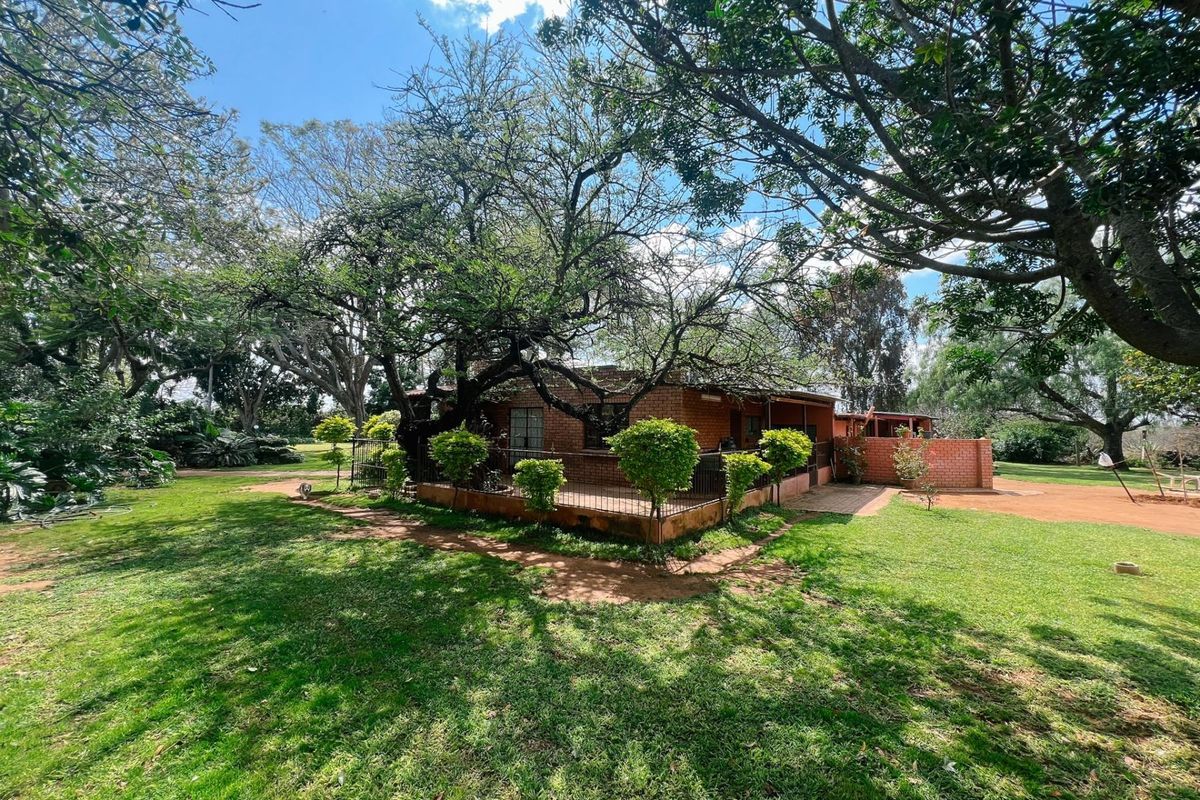 Rear view of a brick farmhouse featuring a covered patio area, surrounded by mature trees and expansive lawn space.