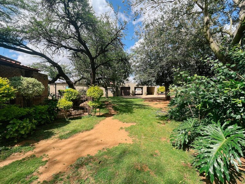 A spacious garden area featuring mature trees, established lawn, and a view towards the property's garage and exterior brick walls.