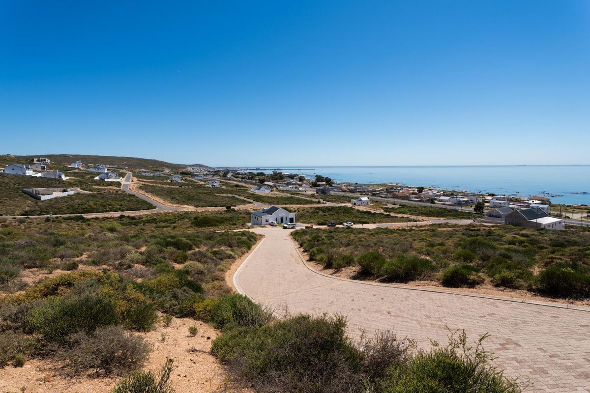 An elevated aerial view of a coastal residential area featuring a paved driveway leading towards a house with ocean views.