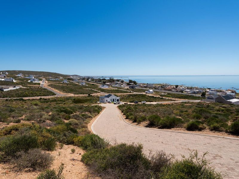 An elevated aerial view of a coastal residential area featuring a paved driveway leading towards a house with ocean views.