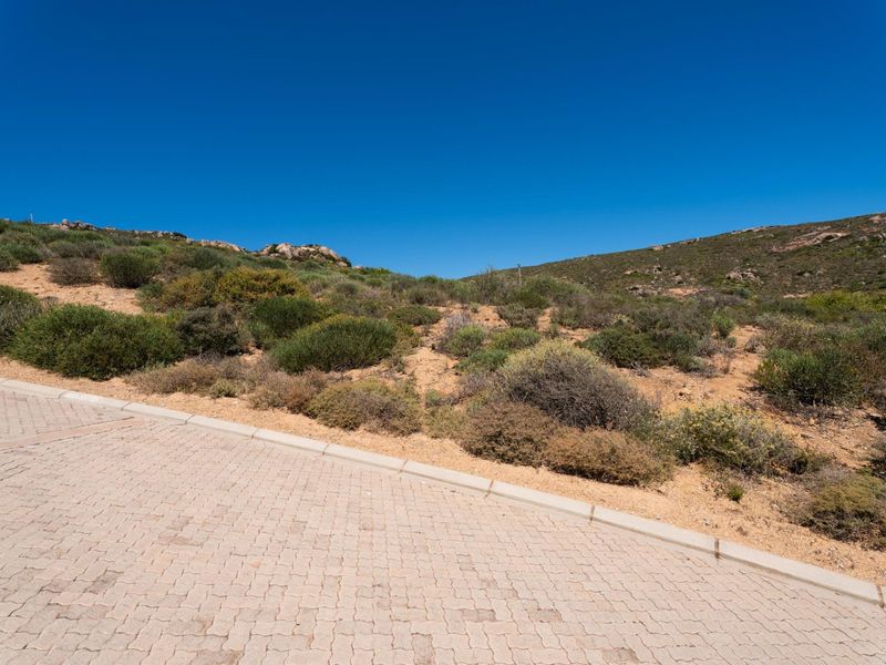 A view of a vacant residential plot featuring a paved driveway and concrete curbing, set against a natural hillside landscape.