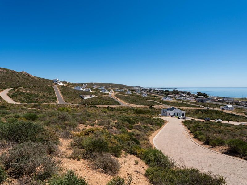 An elevated aerial view of a residential development site featuring paved roads and coastal landscape views.
