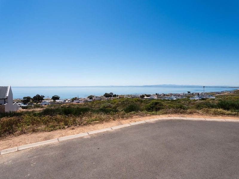 A clear, elevated view of the coastline and surrounding residential area from a paved road.