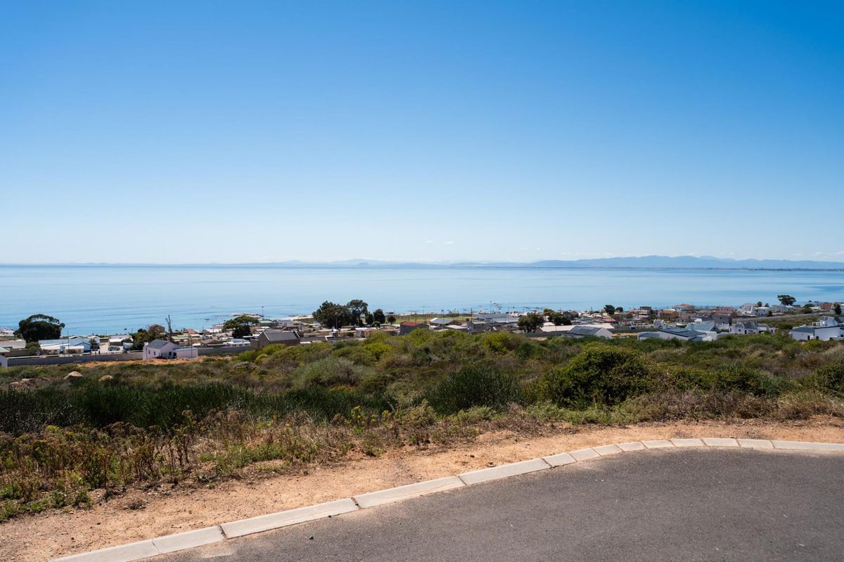 A scenic elevated view overlooking the coastal town and ocean, featuring a paved road and curbing in the foreground.