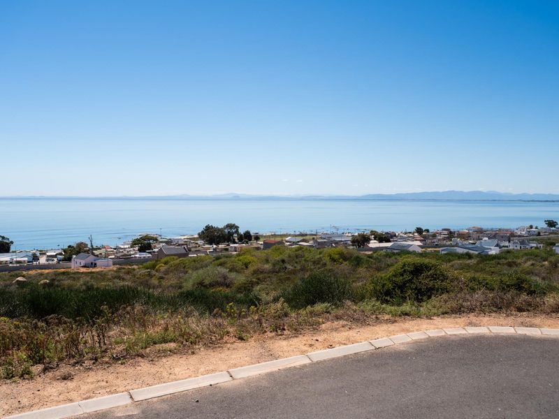 A scenic elevated view overlooking the coastal town and ocean, featuring a paved road and curbing in the foreground.