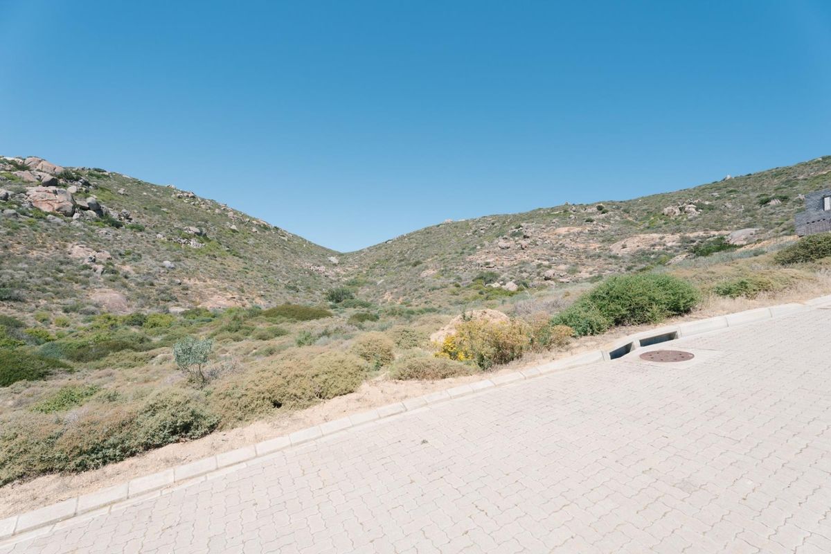A view of the paved street and curbing adjacent to the vacant residential land, featuring natural hillside terrain in the background.