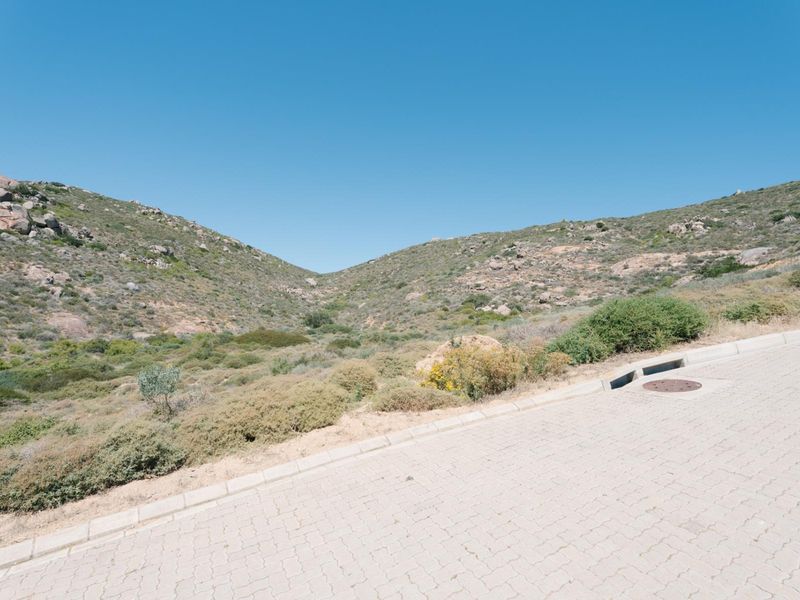 A view of the paved street and curbing adjacent to the vacant residential land, featuring natural hillside terrain in the background.