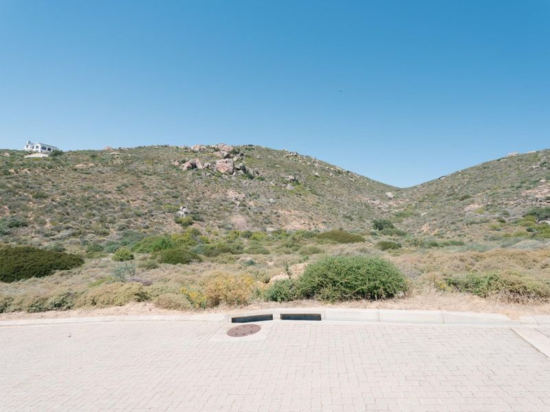 A view of the paved street frontage and stormwater infrastructure, looking out towards the natural hillside landscape.