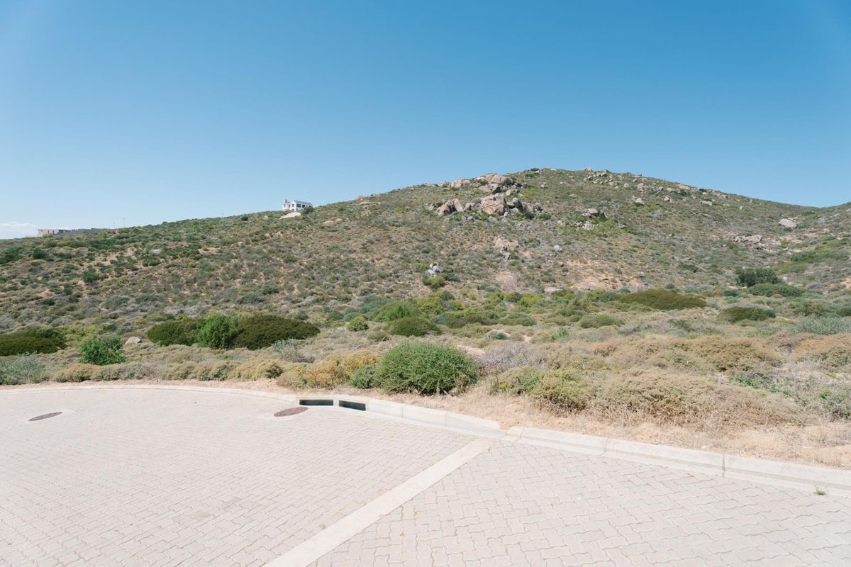 A view of the paved street frontage and stormwater infrastructure leading towards the natural hillside landscape of the vacant residential land.