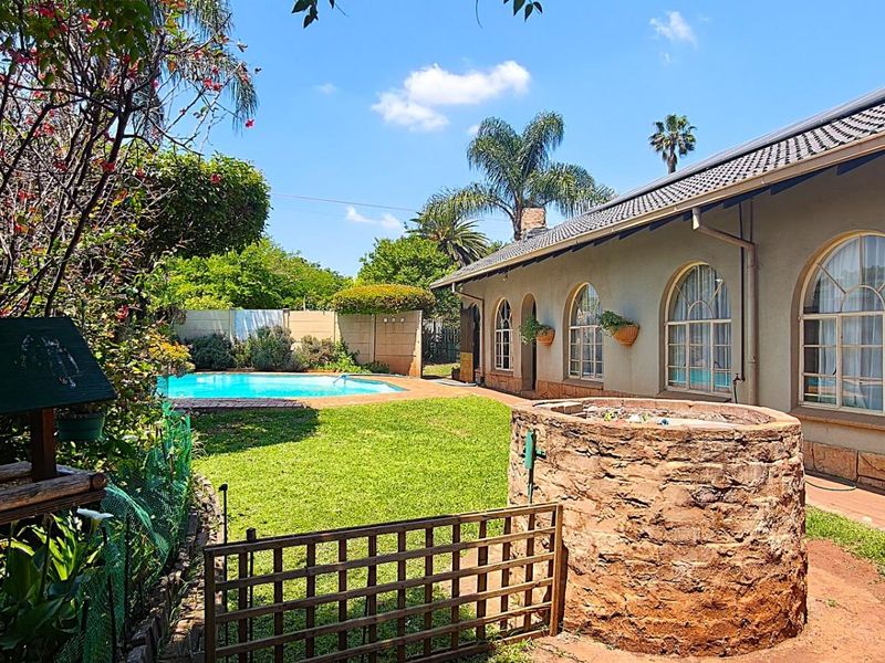 Rear garden view featuring a swimming pool, manicured lawn, stone feature wall, and a house exterior with distinctive arched windows and stone cladding.
