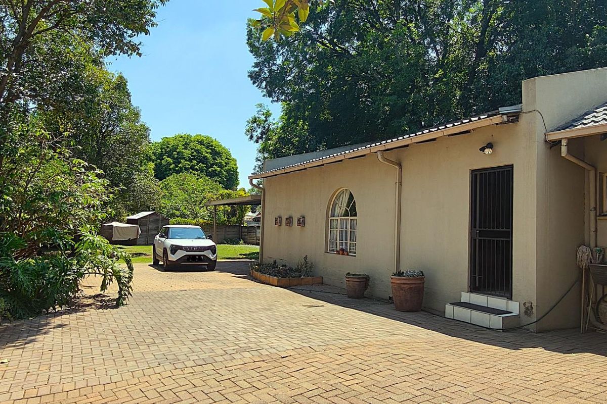 Rear exterior view featuring a paved driveway, established garden, and a functional utility sink area attached to the main building structure.