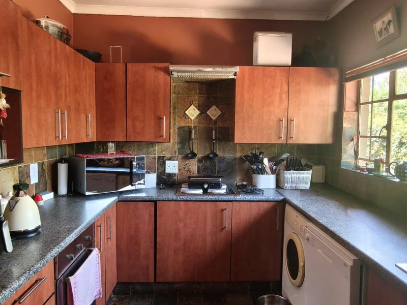 A functional kitchen featuring wood-look cabinetry, stone tile backsplash, granite countertops, and integrated appliances, offering a practical layout with natural light.