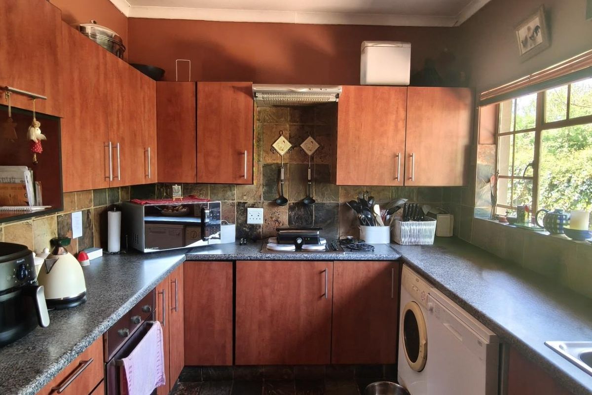 A functional kitchen featuring wood-look cabinetry, stone tile backsplash, granite countertops, and integrated appliances, offering a practical layout with natural light.