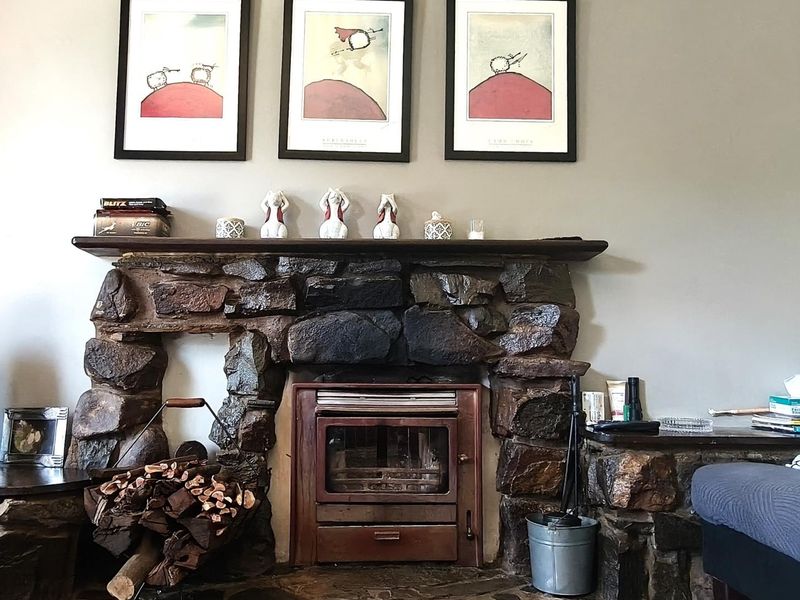 A rustic living room featuring a prominent stone fireplace with a built-in wood burning stove and a timber mantelpiece.