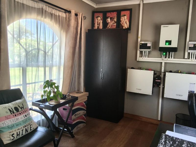 A functional utility space featuring a wall-mounted solar inverter and battery storage system, complemented by an arched window and laminate flooring.