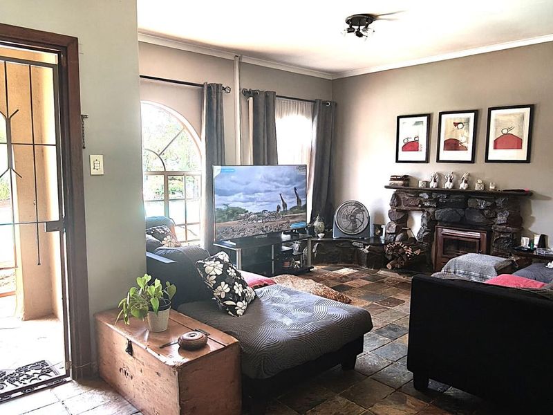 Spacious living room featuring rustic slate tile flooring, a prominent stone fireplace, and an arched window providing natural light.