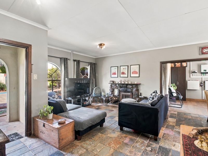 Spacious living room featuring a rustic stone fireplace, durable slate tile flooring, and an arched window providing natural light and access to the patio.