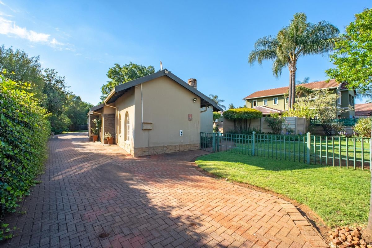A view of the rear exterior featuring a paved driveway, manicured lawn, and metal perimeter fencing surrounding the property.