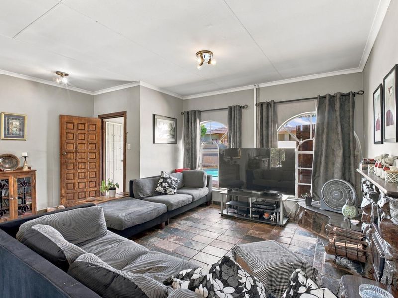 A living room featuring a stone fireplace, tiled flooring, and arched windows that provide natural light and a view of the outdoor area.