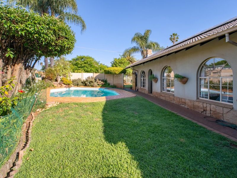 Rear garden view featuring a swimming pool, brick paved patio, and a house exterior with arched windows and stone cladding details.