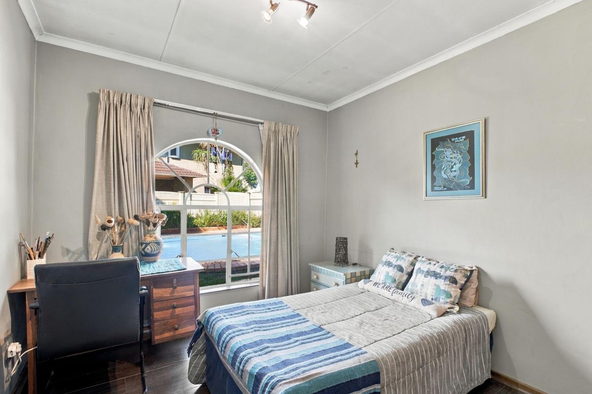 A bedroom featuring laminate flooring and a distinctive arched window with views of the pool area.