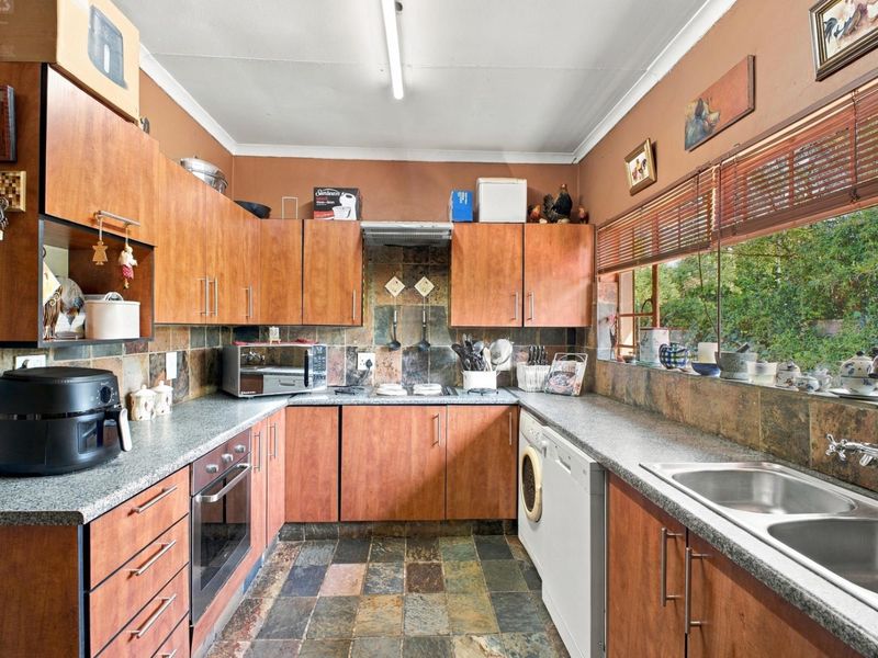 A functional kitchen featuring wood-look cabinetry, slate tile flooring, a built-in oven, and a double bowl sink with ample natural light from the window.