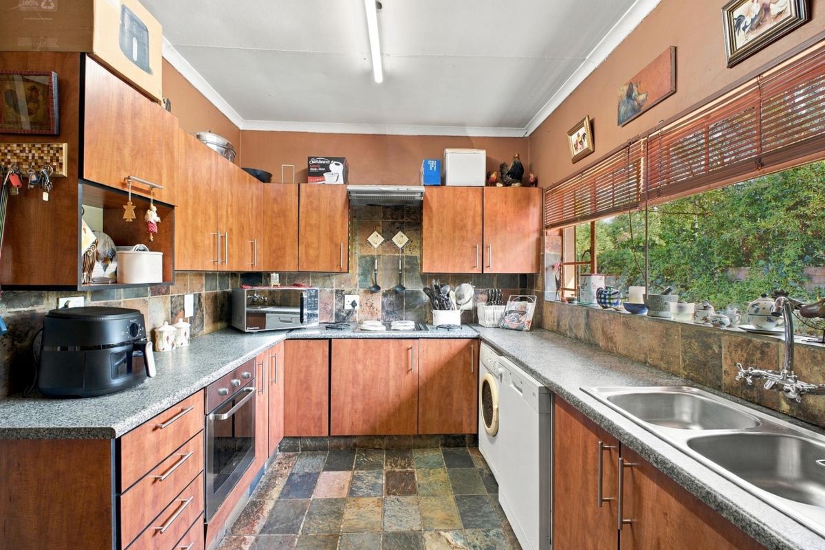 A functional kitchen featuring wood-look cabinetry, slate tile flooring, a built-in oven, and a double bowl sink with ample natural light from the window.