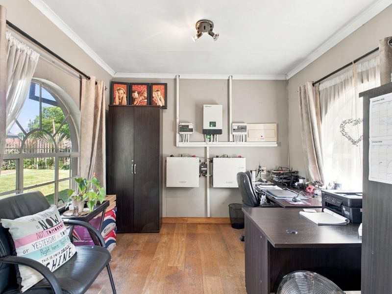 A functional home office featuring timber flooring, an arched window, and a wall-mounted solar power system with battery storage.