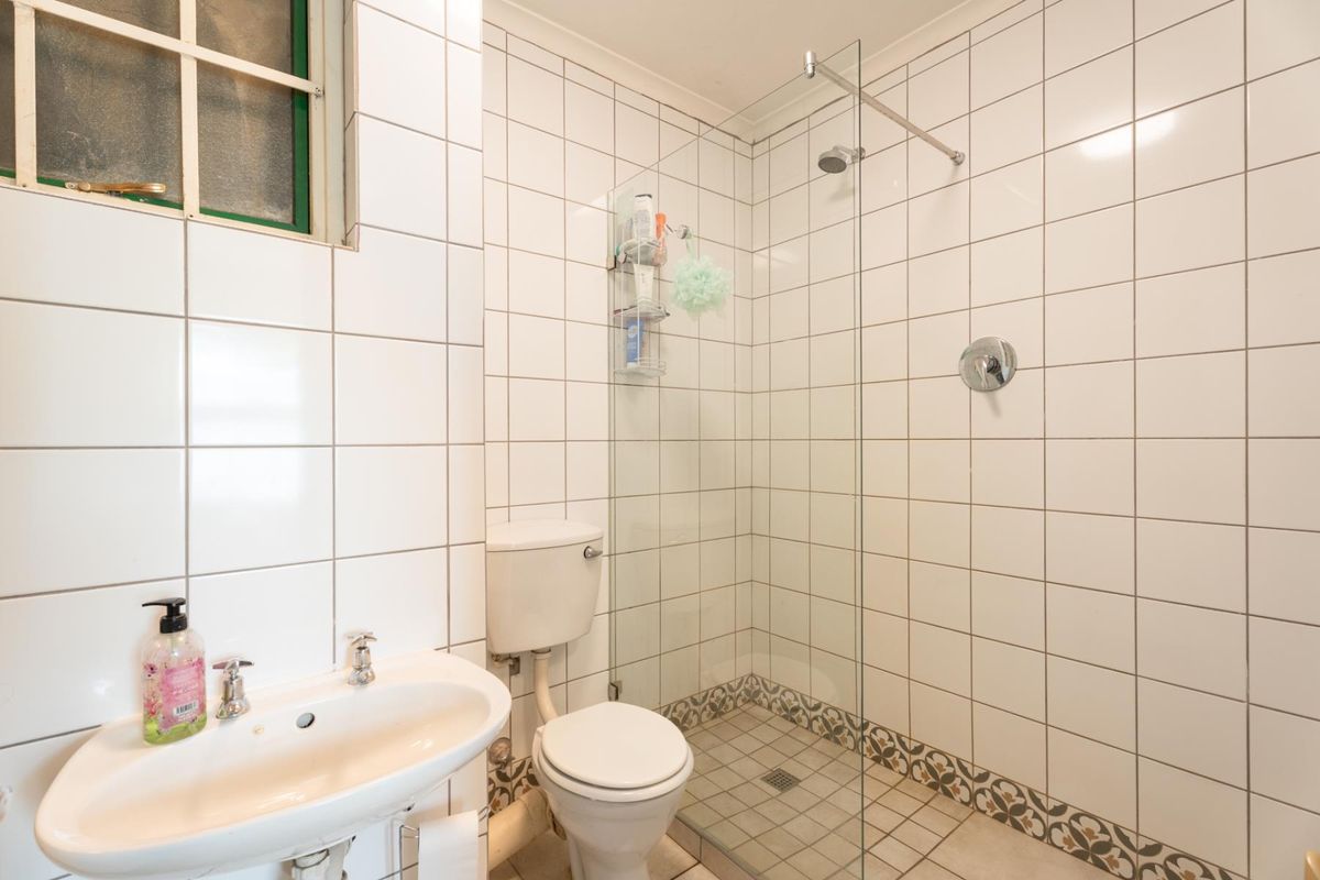 A functional bathroom featuring a walk-in shower with a glass screen, pedestal basin, and toilet, finished with white wall tiles and decorative floor accents.