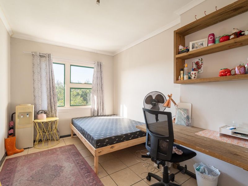 A functional bedroom featuring tiled flooring, a window for natural light, and built-in wooden shelving.