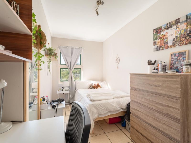 A compact bedroom featuring tiled flooring, a window for natural light, and a standard ceiling light fixture.