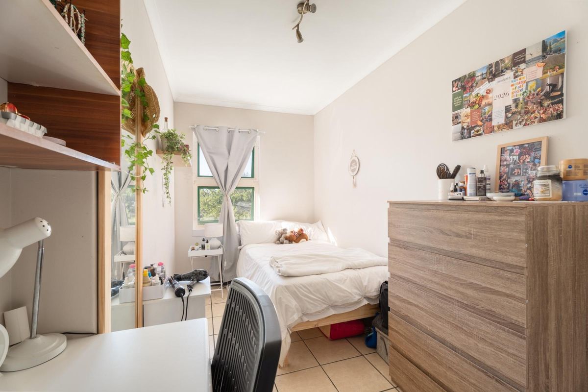 A compact bedroom featuring tiled flooring, a window for natural light, and a standard ceiling light fixture.