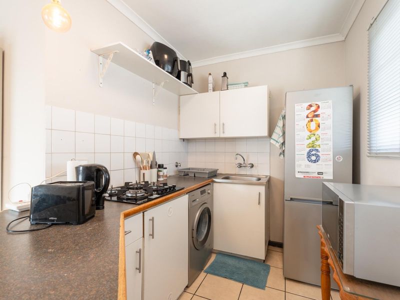 Compact kitchen featuring a gas hob, built-in cabinetry, laminate countertops, and a stainless steel sink with tiled splashback and flooring.