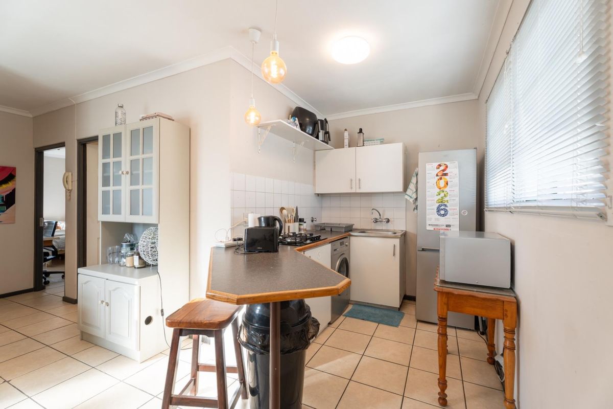 Compact kitchen featuring tiled flooring, built-in cabinetry, a breakfast bar, and integrated hob, offering a functional layout for an apartment setting.