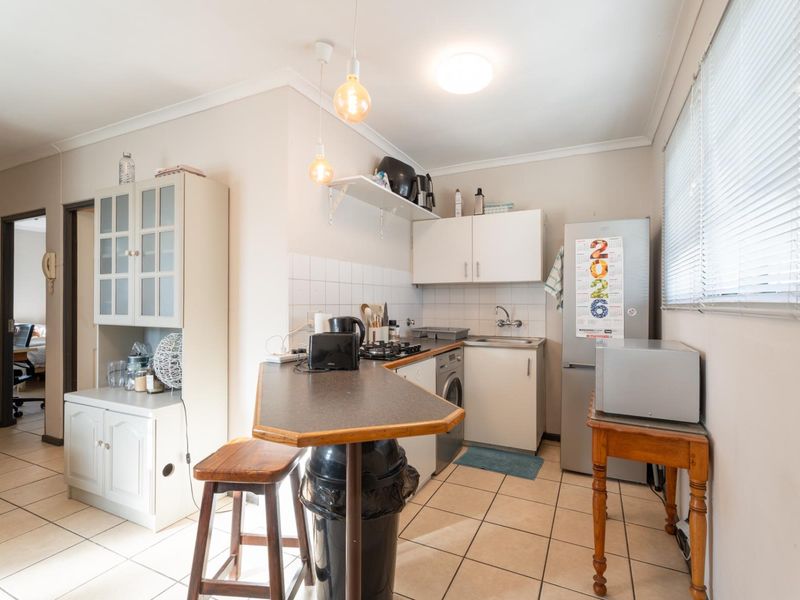 Compact kitchen featuring tiled flooring, built-in cabinetry, a breakfast bar, and integrated hob, offering a functional layout for an apartment setting.