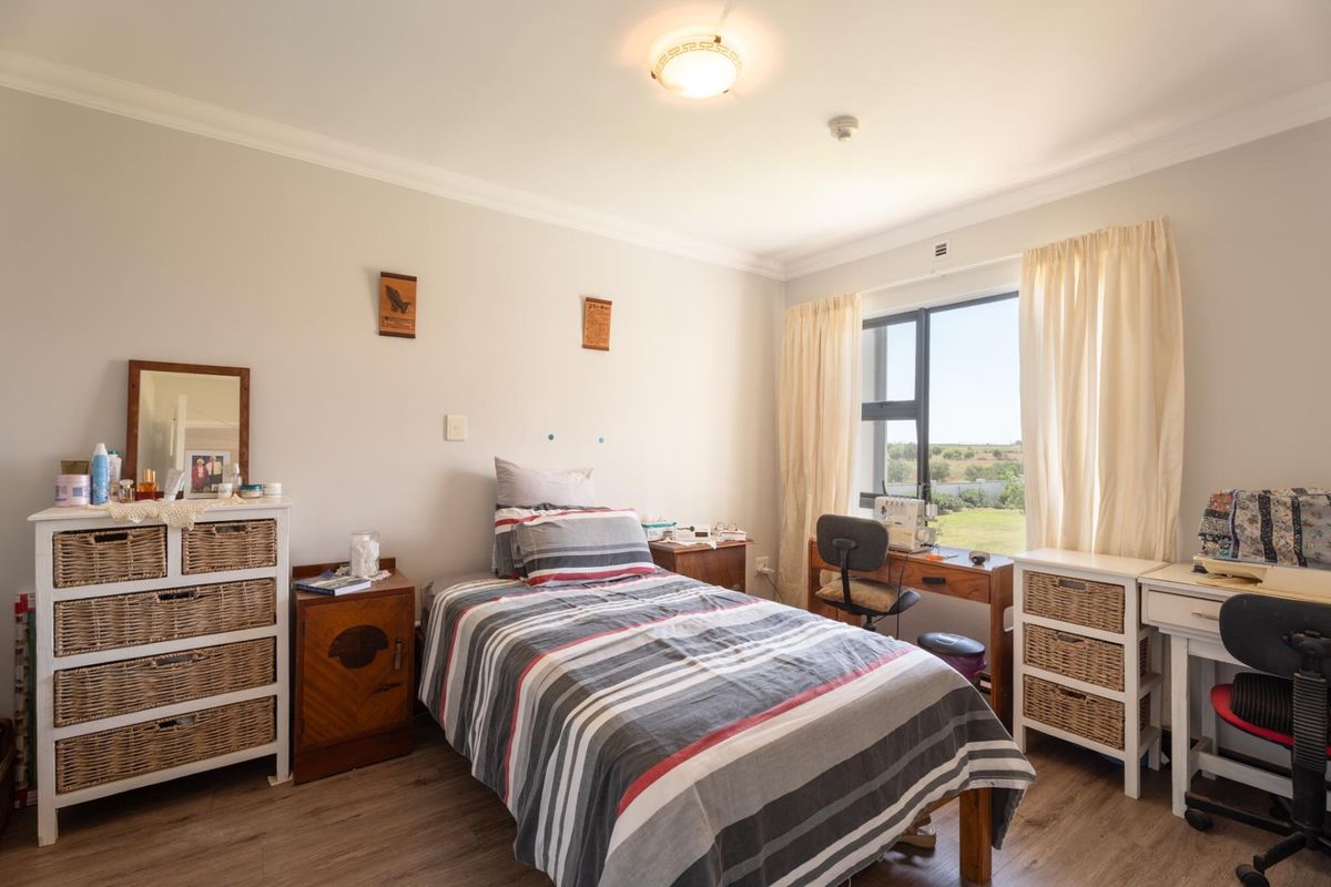 A well-lit bedroom featuring laminate flooring, neutral wall tones, and a window providing natural light and exterior views.
