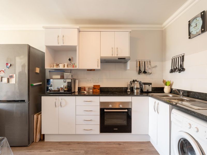 A well-maintained kitchen featuring white cabinetry, granite countertops, a built-in oven, electric hob, extractor fan, and integrated space for laundry appliances.