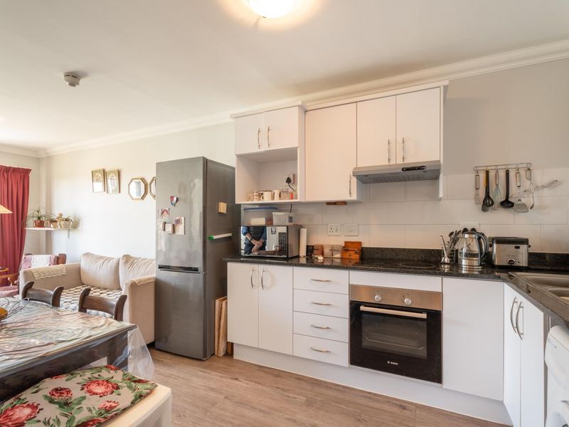 An open-plan living and kitchen area featuring white cabinetry, granite countertops, integrated appliances, and durable laminate flooring.