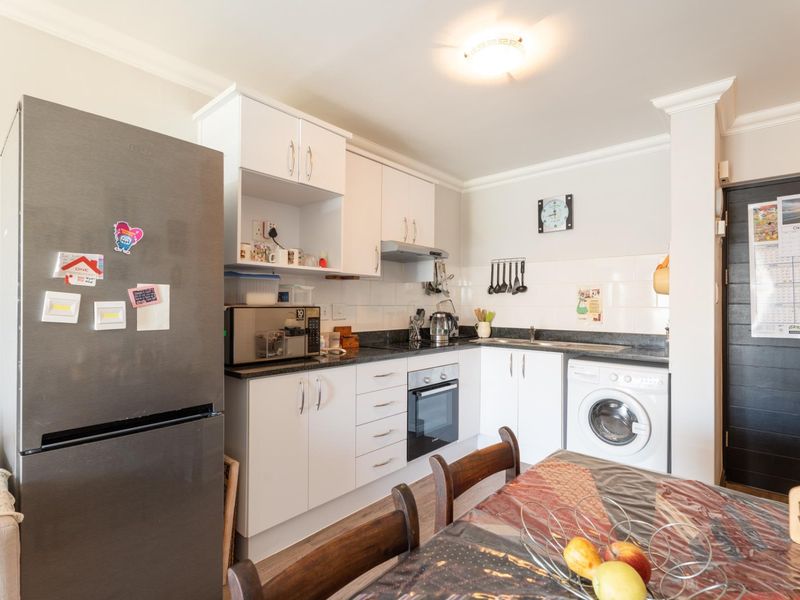 Compact kitchen featuring white cabinetry, granite countertops, built-in oven and hob, tiled backsplash, and integrated laundry plumbing.