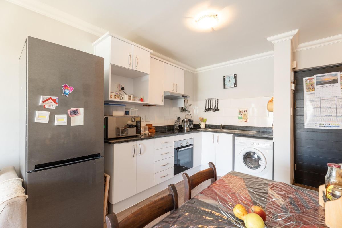 Compact kitchen featuring white cabinetry, granite countertops, built-in oven and hob, tiled backsplash, and integrated laundry plumbing.