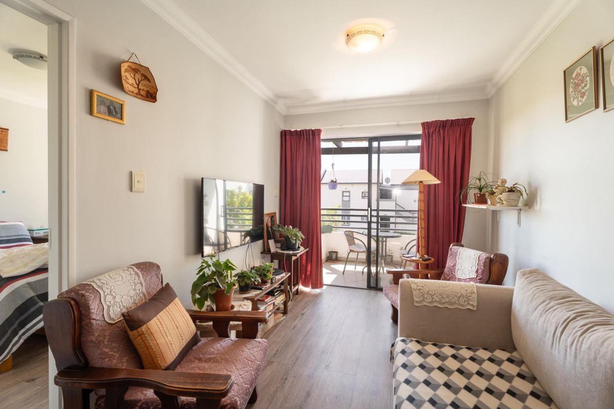 A cozy living room featuring laminate flooring and a sliding glass door that opens onto a private balcony, providing natural light.
