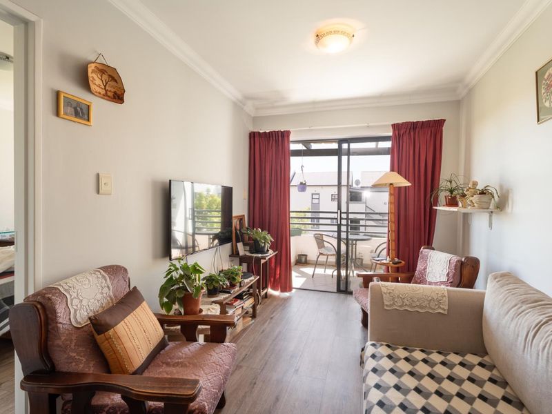 A cozy living room featuring laminate flooring and a sliding glass door that opens onto a private balcony, providing natural light.