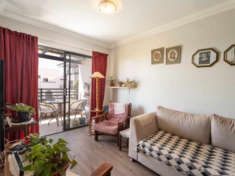 A comfortable living room featuring laminate flooring, ceiling cornice, and a large sliding glass door providing access to an attached balcony.